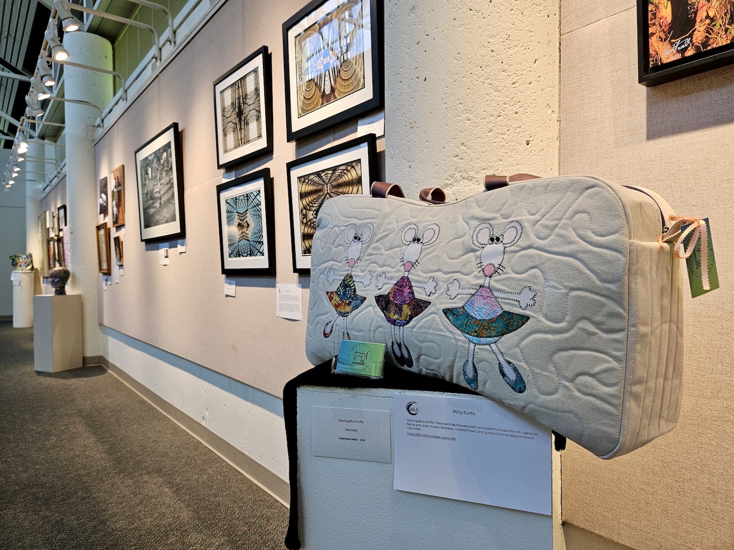 A GALA art exhibit inside Gresham City Council Chambers featuring an ornate bag on a pedestal in front of a wall of paintings